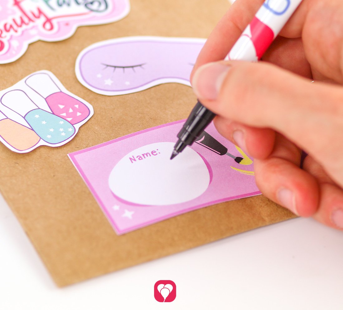 Mit einem schwarzen Filzstift wird das Namensschild im Design der balloonas Beauty Party Geschenkaufkleber beschriftet.