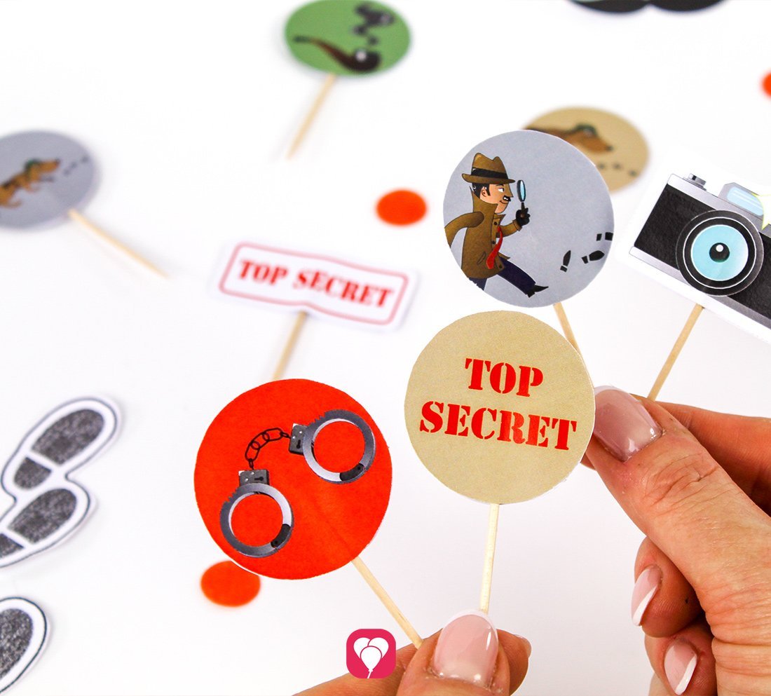 Eine Person hält mehrere selbstgebastelte Schilder im Design der ballonas Detektiv Deko Picker. Motive: Handschellen, ein Detektiv mit einer Lupe und TOP SECRET.