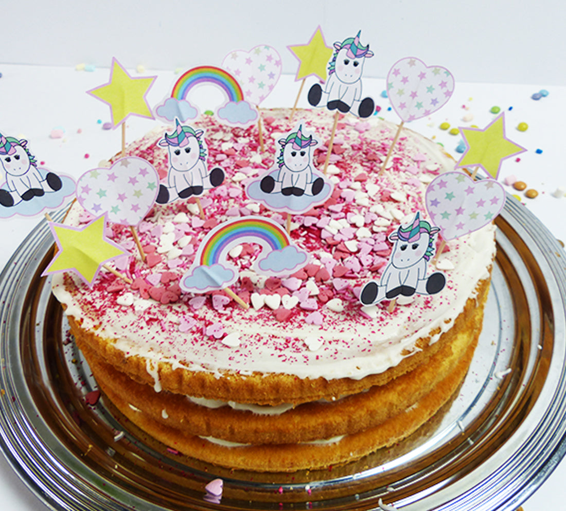 Eine Sahne-Torte mit bunten Herzstreuseln. Auf der Torte sind außerdem zahlreiche Einhorn Deko Picker, selbstgebastelt mit der Vorlage von balloonas, eingesteckt.