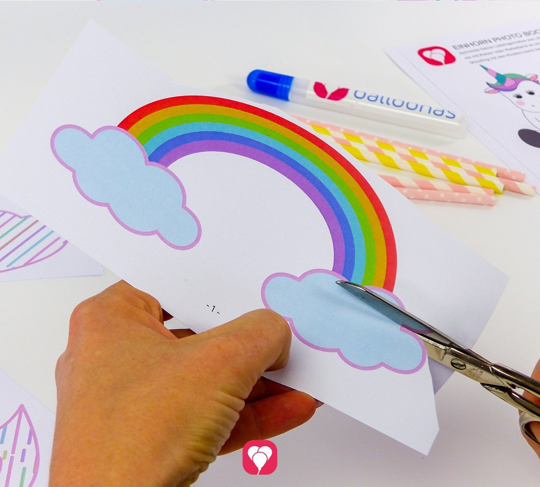 Eine Person schneidet ein Regenbogen-Motiv aus dem Bastelvorlagen Set "Einhorn Photo Booth" aus.