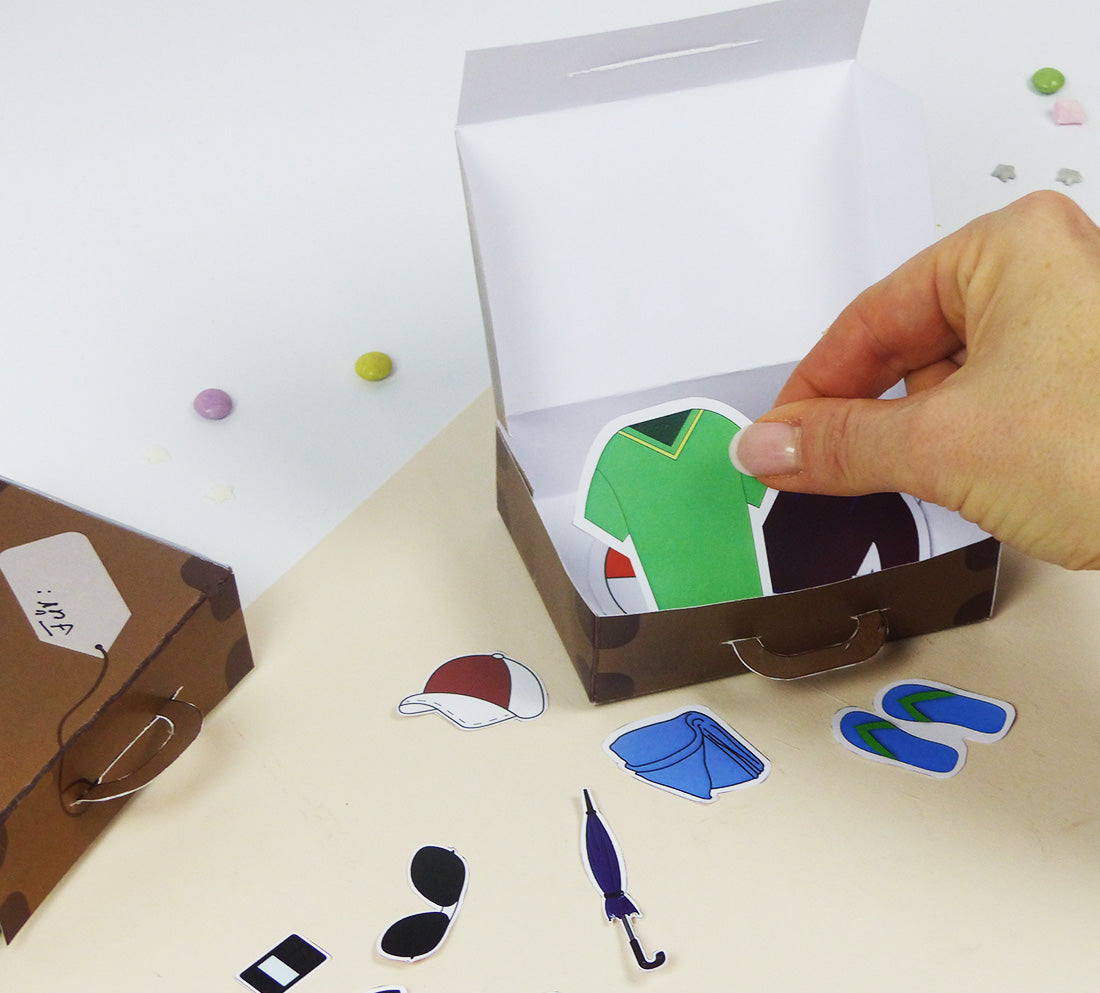 Die einzelnen Motive vom DIY-Spiel "Ich packe meinen Koffer" von balloonas können während dem Spiel in den Koffer gelegt werden. Zu sehen sind ein T-Shirt, eine Mütze, Flip Flops, Sonnenbrille, Regenschirm und ein Handtuch.