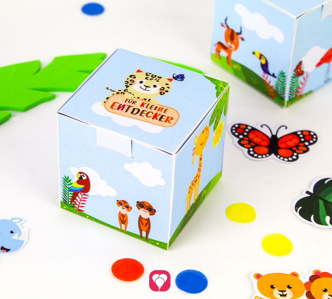 Fertiggebastelte Geschenkbox zum Motto "Safari" von balloonas. Daneben liegen Papier-Schmetterlinge und buntes Konfetti. Auf der Geschenkbox sind Tiermotive abgebildet und der Text "Für kleine Entdecker".