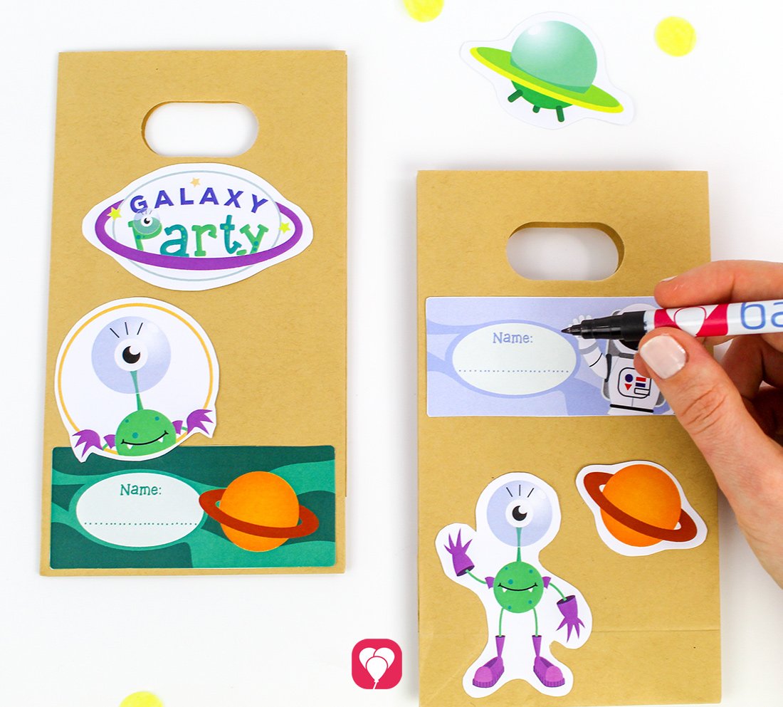 Zwei mit den balloonas Weltraum Gescehnkaufklebern dekorierte Geschenktüten. Auf der rechten Tüte wird ein Namensschild mit einem Filzstift beschriftet. 